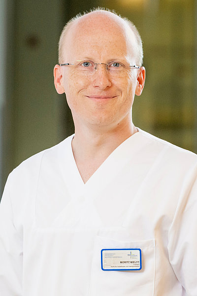 Älterer Mann in weißer medizinischer Arbeitskleidung mit Namensschild