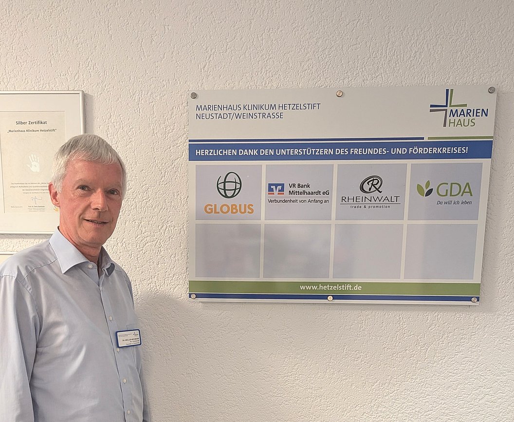 Mann steht neben einer Wand mit einem Schild des Marienhaus Klinikums Hetzelstift Neustadt/Weinstrasse und Logos von Unterstützern wie Globus, VR Bank, Rheinwalt und GDA