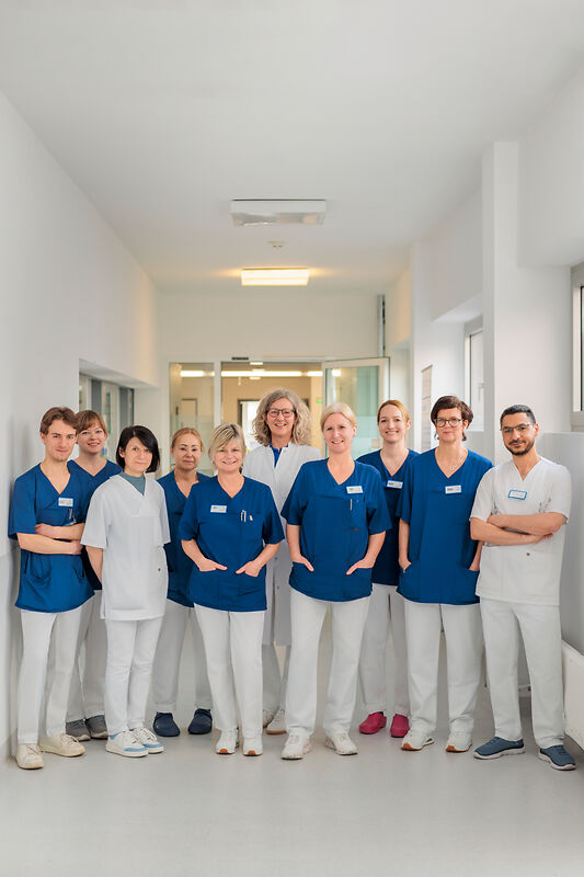 Gruppe von medizinischem Personal in blauer und weißer Arbeitskleidung steht in einem hellen Krankenhausflur